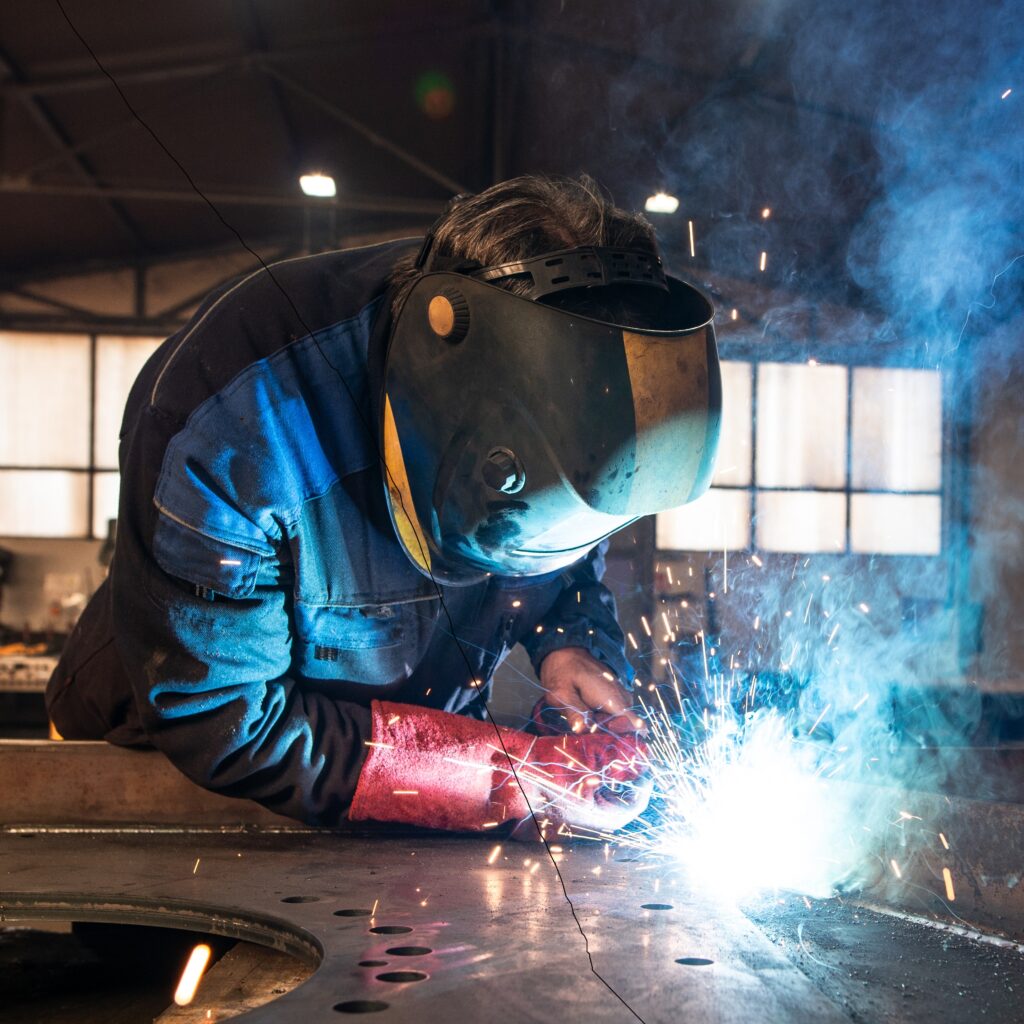 Professional industrial welder welding metal parts in metalworking factory.